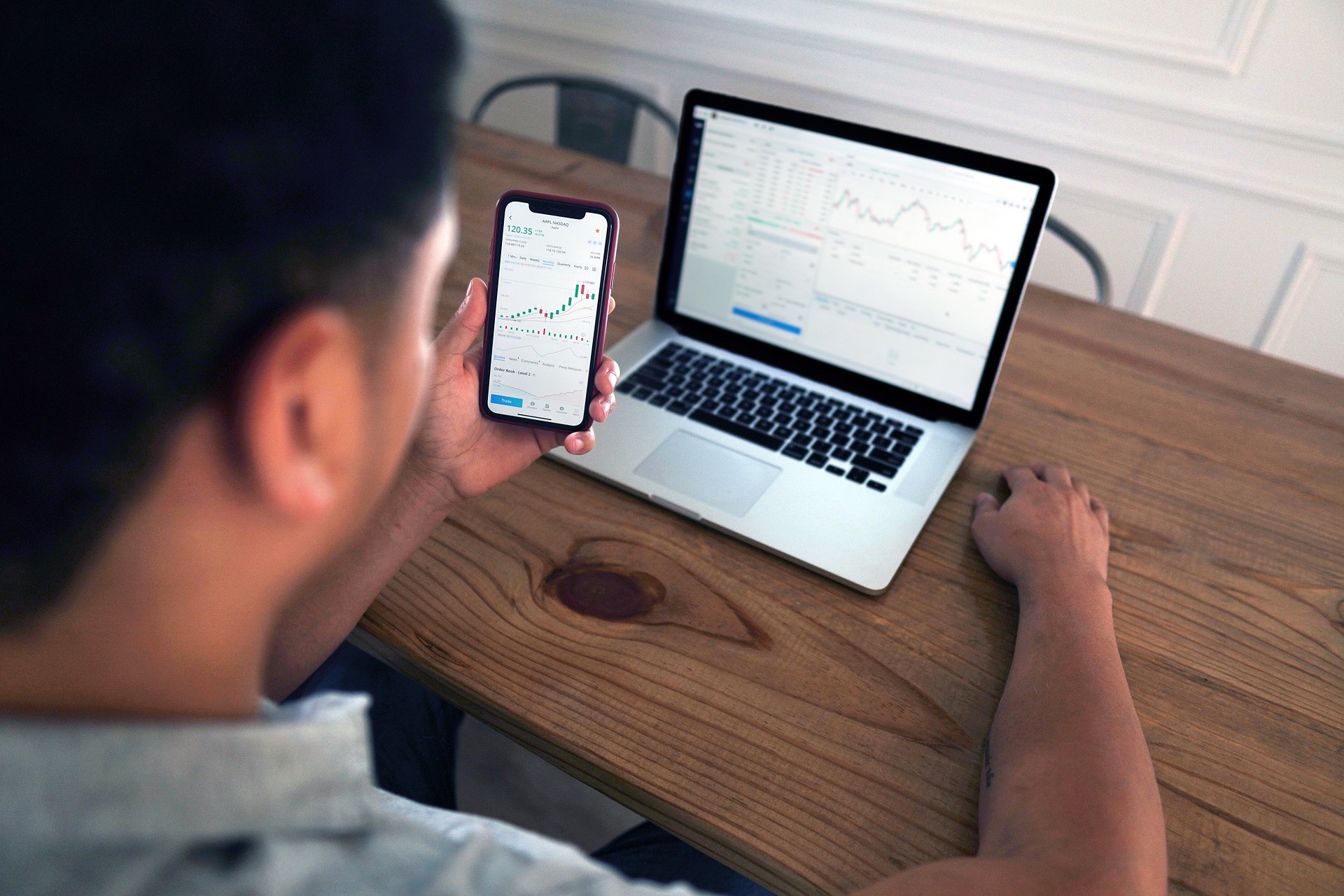 Man following stocks on computer and phone sitting at desk