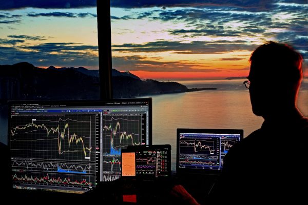 Man looking at screens monitoring stocks in front of office window
