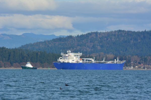 Oil tanker boat with tugboat pulling it and mountains in distance